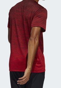 Camiseta atlética roja de manga corta con un patrón texturizado, cuello redondo y un dobladillo trasero ligeramente más largo. Llevada con pantalones cortos negros.