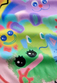 Bunt gemusterter Stoff mit verspielten, abstrakten Designs, darunter lächelnde Gesichter, Formen und lebendige Texturen in Grüntönen, Gelb und Blau.