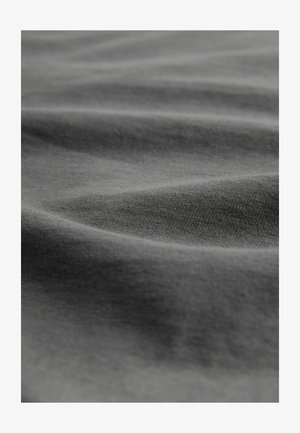 Minkštas, tamsiai pilkas audinys su subtiliais raukšlėmis ir matoma smulkių mezgimų tekstūra artimesniame vaizdą.