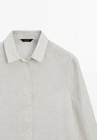 Chemise beige clair à manches longues avec boutons, col classique et texture subtile à rayures verticales.