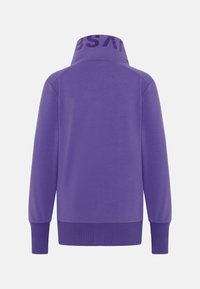 Sweat violet à manches longues avec poignets et ourlet côtelés, comportant un col montant avec des lettres sombres partiellement visibles.
