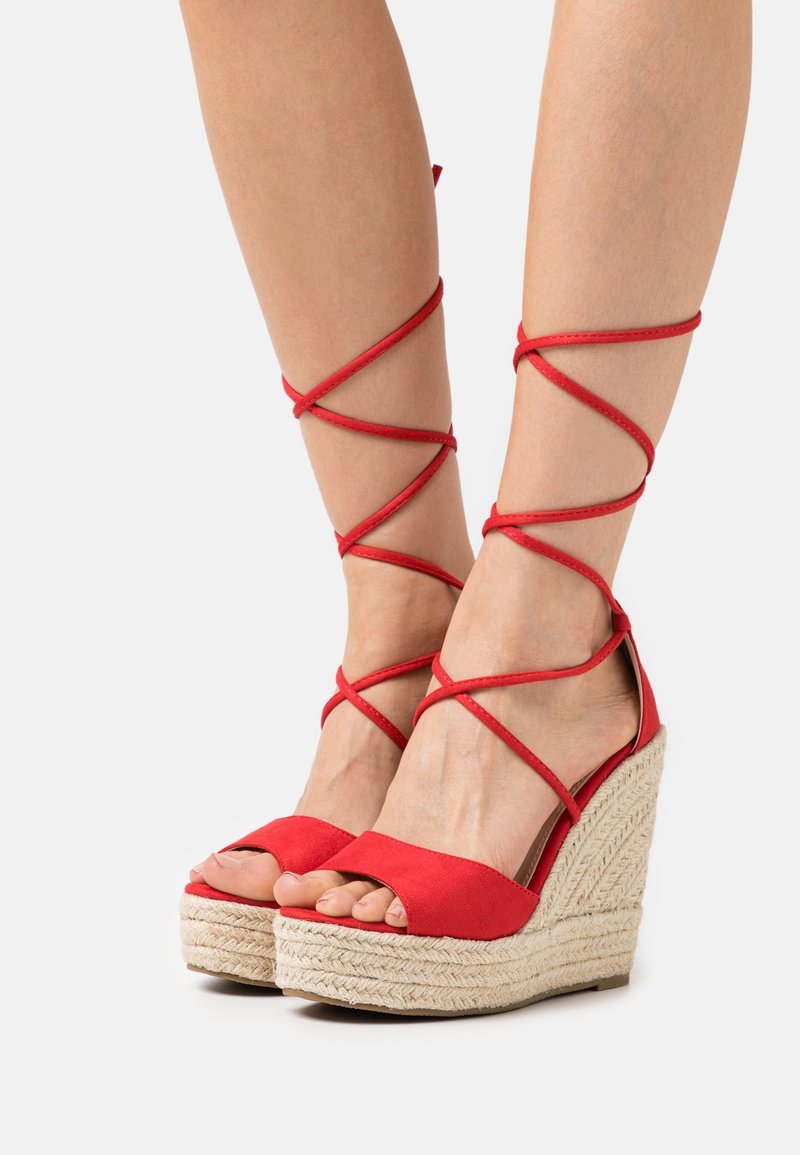 Sandali con tacco a cuneo rossi con design open-toe e lacci avvolgenti alla caviglia. Realizzati in tessuto morbido con una piattaforma intrecciata in juta e un tacco texture.