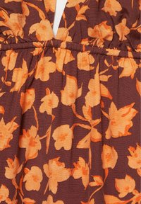 Tissu marron avec motif floral orange et couture élastique froncée à la taille sur un vêtement.