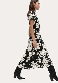 Czarna sukienka w kwiaty z białymi kwiatami, krótki rękaw i zwiewny dół. Noszona z czarnymi, wysokości kolan butami i dopasowaną w talii.
