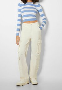 Ljuskrämfärgade cargobyxor med flera fickor, kombinerade med en figursydd blåvit randig crop top. Mjukt bomullsmaterial, avslappnad passform.