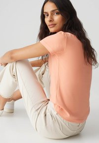 T-shirt pesca a maniche corte in morbido tessuto, con colletto rotondo e vestibilità rilassata, abbinata a jeans cropped di colore crema.