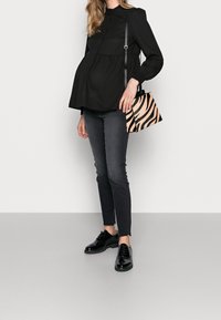 Blusa nera a maniche lunghe con vita arricciata, abbinata a jeans scuri e scarpe nere in vernice. Tiene in mano una piccola borsa a strisce di zebra.