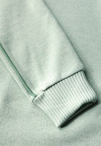 Jasnozielony materiał na bluzę z ryflowanymi mankietami i gładką teksturą, z subtelnym pionowym wzorem w paski na powierzchni.