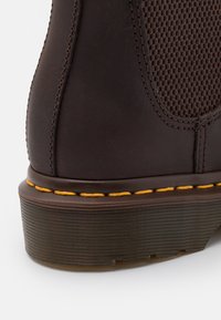 Mörkbrun ankelboot med texturerad nätpanel, gult stygn och gummisula med räfflat mönster för bra grepp.