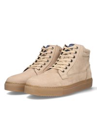 Beige suède hoge sneakers met vetersluiting aan de voorkant, ronde neus en een gumrubberen zool. Kenmerken zijn gestikte details en een gewatteerde kraag.