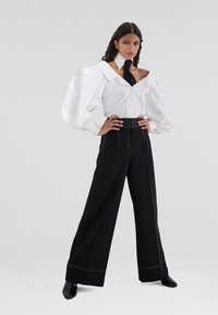 Camicia bianca oversize con ampie maniche a sbuffo, abbinata a pantaloni larghi neri con cuciture a contrasto e vita alta.