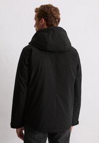 Zwart hoodiejack met een gladde, matte afwerking. Voorzien van zijnaden en verstelbare manchetten. Draagt over donkere jeans met een subtiel design.