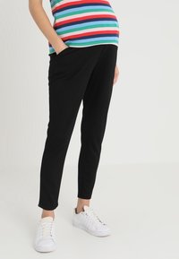 Zwarte slim-fit broek met zijzakken, gecombineerd met witte sneakers. Het shirt heeft horizontale strepen in rood, blauw, groen en wit.