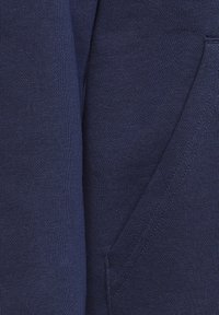 Mörkblå bomullstyg med en slät yta och ribbdetaljer. Inkluderar en sidficka med en ren finish.