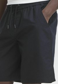 Shorts noirs en tissu léger, avec une taille élastique à cordon de serrage, des poches latérales et une coupe décontractée.
