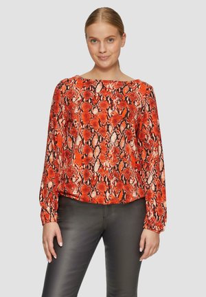 Rode slangenprint blouse met lange, pofmouwen, ronde hals en een losse pasvorm. Gecombineerd met zwarte slim-fit broek.