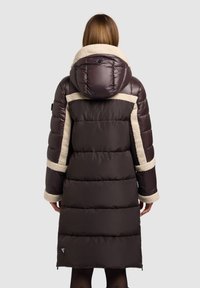 Piumino lungo in marrone scuro, con cappuccio e polsini foderati in crema soffice, design trapuntato e lunghezza fino a metà coscia.