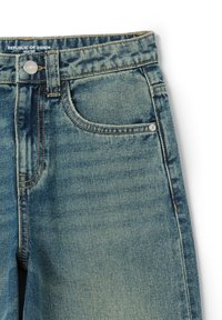 Jeans de mezclilla azul claro con un acabado deslavado, diseño de cinco bolsillos, herrajes de botón de latón y costuras en contraste a lo largo de las costuras.