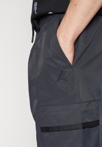 Graue Cargo-Hosen mit glatter Textur, seitlichen Taschen, einem elastischen Bund und einem schwarz gestickten Logo nahe der Tasche.