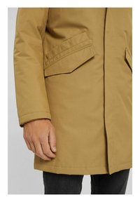Beżowa, funkcjonalna kurtka o gładkiej fakturze, z dwoma przednimi kieszeniami i prostym krojem. Tkanina jest lekka i wodoodporna.