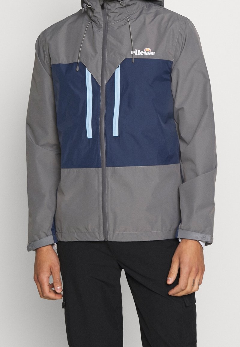 Męska kurtka w kolorze szarym i granatowym, z kapturem, zamkiem błyskawicznym, niebieskimi akcentami oraz geometrycznym wzorem bloków kolorystycznych. Lekka i wodoodporna.