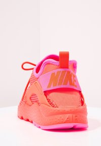 Tenisky Nike Air v živých růžových a oranžových odstínech, s materiálem z prodyšné síťoviny, polstrovaným límcem a páskem na patě s logem a texturovanými detaily.