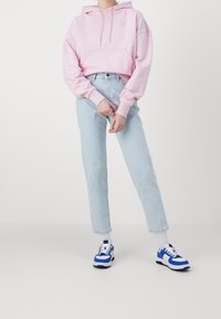 Sudadera con capucha de color rosa claro y bolsillo frontal, combinada con jeans de tiro alto azul claro y zapatillas blancas y azules.