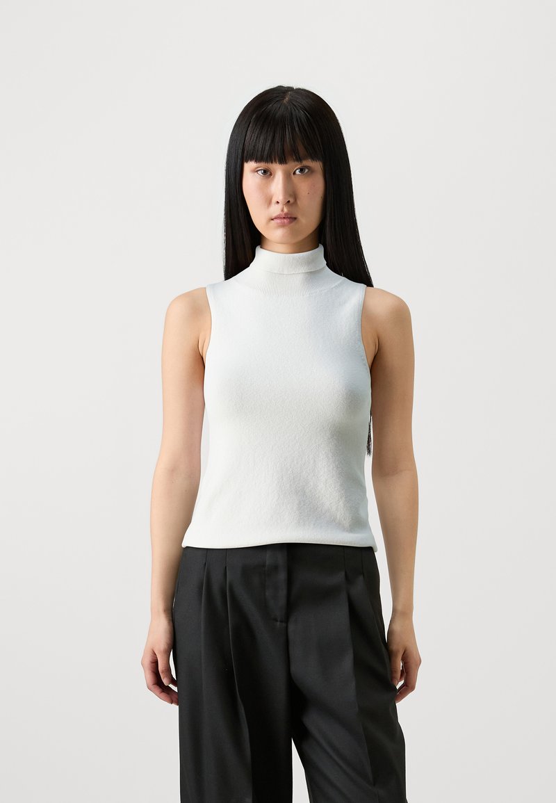 White sleeveless top featuring a high neck, fitted design, and textured fabric. Worn with black high-waisted trousers for contrast.