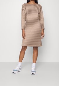 Beige raido-kleid mit langen Ärmeln, Boot-Ausschnitt und lockerer Passform; kombiniert mit hellblauen und weißen Sneakern. Glatte Baumwollqualität.
