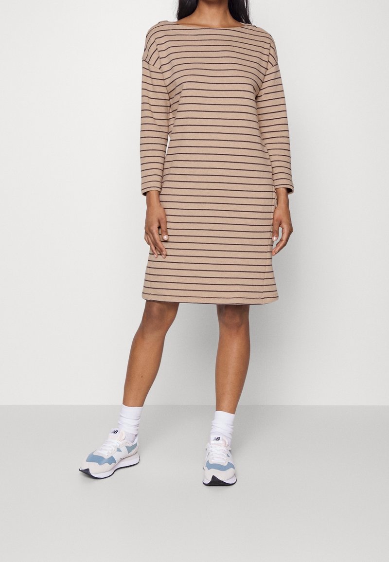 Beige raido-kleid mit langen Ärmeln, Boot-Ausschnitt und lockerer Passform; kombiniert mit hellblauen und weißen Sneakern. Glatte Baumwollqualität.