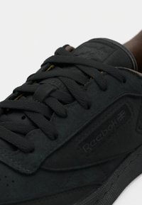 Tuvo plāna melnā Reebok sporta apava ar strukturētām auklām, izteiksmīgu šuvju un Reebok logotipu ar Apvienotās Karalistes karogu sānu paneļa daļā.
