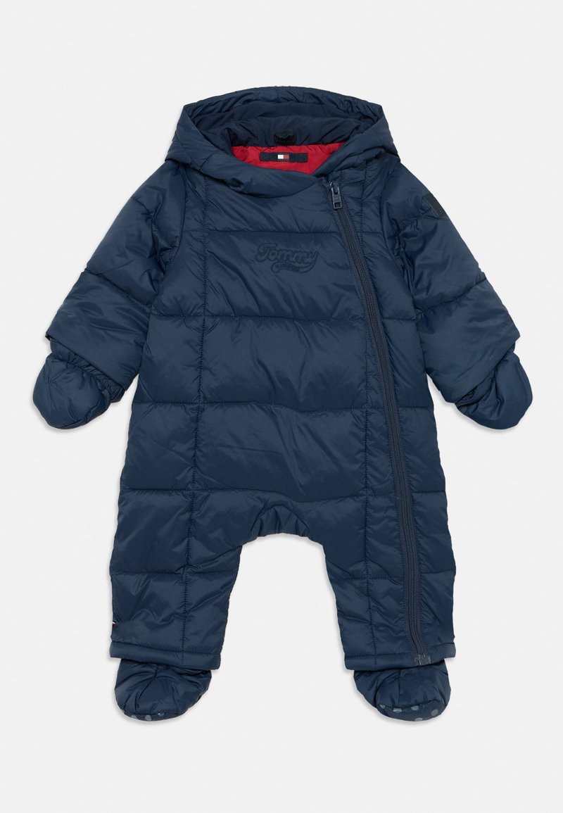 Jūras zilas polsterētas sniega uzvalks ar rāvējslēdzēju, noņemamu kapuci un pārklātiem zābakiem. Iezīmējas ar kviltotu tekstūru un logotipa detaļu uz krūtīm.