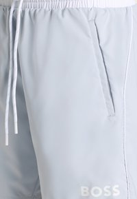 Világoskék rövidnadrág sima anyagból, rugalmas derékpánttal, fehér húzózsinórral és oldalzsebekkel. Fehér "BOSS" logóval.