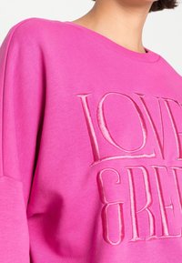 Fuchsiová mikina se kulatým výstřihem, s výšivkou textu "LOVE" a "GREAT" ve sladěné světle růžové barvě. Měkký materiál, volný střih.