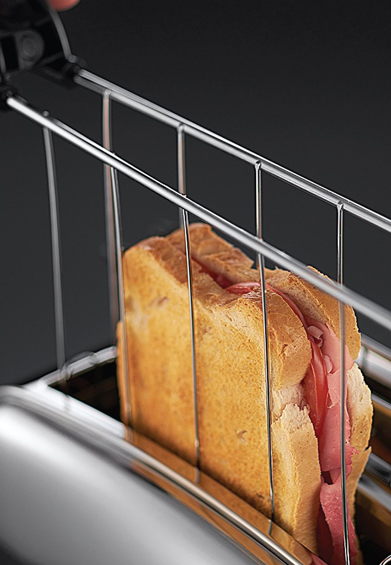Edelstahl-Toaster mit einem geschnittenen Sandwich darin, das aus goldbraunem Brot und rosa Aufschnitt besteht, der durch Drahtschlitze gesichert ist, vor einem dunklen Hintergrund.