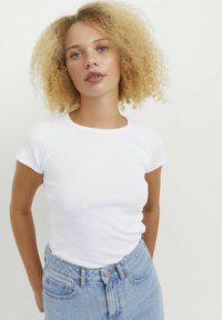 White ribbed short-sleeve t-shirt with a round neckline, paired with light blue high-waisted jeans. The fabric appears soft and textured.