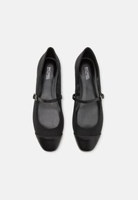 Black Mary Jane flats made of smooth fabric with a round toe, wide elastic strap, and a sleek, glossy black toe cap.