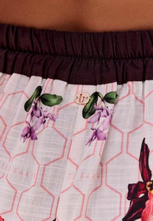 Elastisk taljebånd i mørk lilla over hvidt stof med pink sekskantet mønster og lilla blomstermotiv, med et lille metal logo-tag.