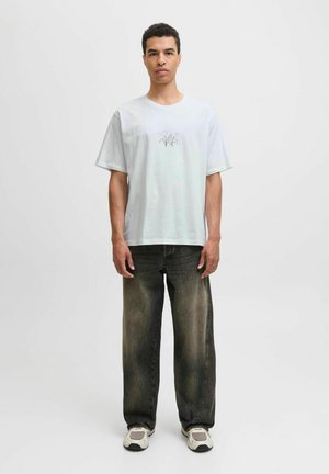 Weißes Baumwoll-T-Shirt mit kurzen Ärmeln, das ein florales Design in Pink und Grün zeigt, kombiniert mit dunkel verblassten, weiten Jeans und grauen Turnschuhen.