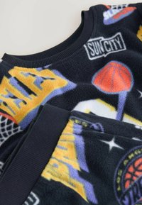 Polarowy sweter w ciemnym granacie z kolorowymi grafikami związanymi z koszykówką i sportem. Posiada ściągacz przy kołnierzu oraz miękką teksturę dla zapewnienia komfortu.