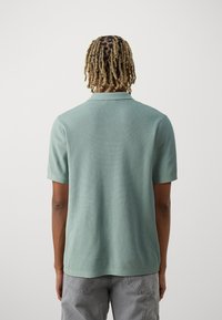 Polo vert clair en tissu texturé avec un col classique, des manches courtes et un ourlet droit, vu de dos.