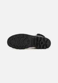 Svart sneakersåle med teksturert gummioverflaten, som har et sikksakk-mønster og definerte spor for grep og feste.