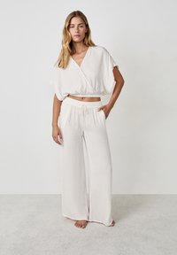 Conjunto holgado de color beige claro que incluye una blusa corta de escote en V con mangas cortas y pantalones de pierna ancha a juego con una cintura elástica.
