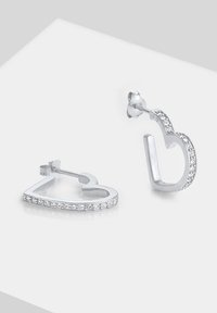 Orecchini a forma di cuore in argento, con una finitura metallica liscia e decorati con cristalli trasparenti lungo il bordo esterno.