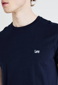 Námořnická modrá bavlněná tričko s krátkým rukávem. Obsahuje kulatý výstřih a bílé vyšívané logo "Lee" na levé hrudi. Měkká textura.