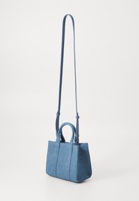 Sac en denim bleu clair avec deux poignées supérieures et une bandoulière ajustable. Forme structurée avec des détails de couture visibles.