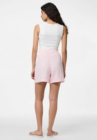 Top a coste bianco abbinato a pantaloni corti leggeri e testurizzati di colore rosa. I pantaloni corti presentano una vita elasticizzata e una vestibilità comoda. Sandali semplici completano il look.