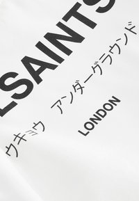 Bijela tkanina s podebljanim crnim tekstom. Tekst uključuje "SVETCI" i "LONDON" s dodatnim znakovima na japanskom. Glatka tekstura, minimalistički dizajn.