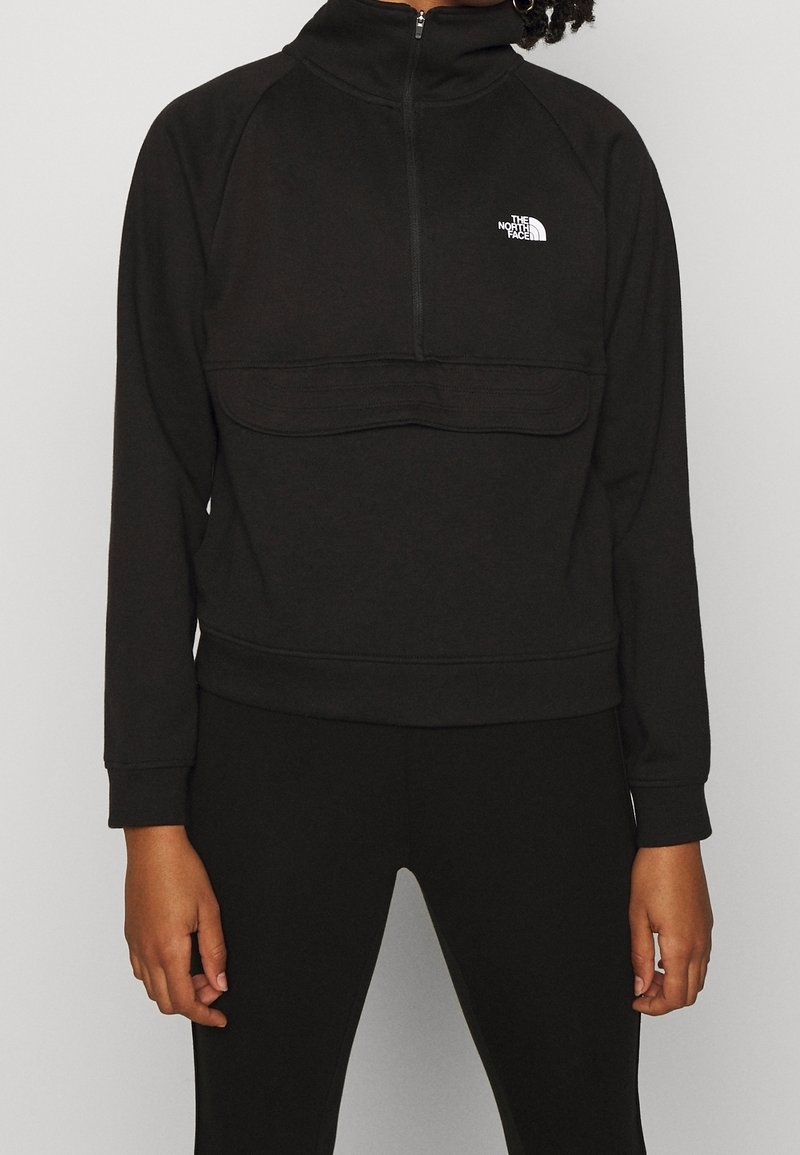 Personne portant un sweat-shirt noir North Face avec fermeture éclair à l'avant et un pantalon noir assorti, vue des épaules aux cuisses.