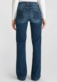 Jeans a zampa d'elefante in denim blu scuro con vita media, due tasche posteriori con motivi cuciti e una finitura pulita all'orlo.
